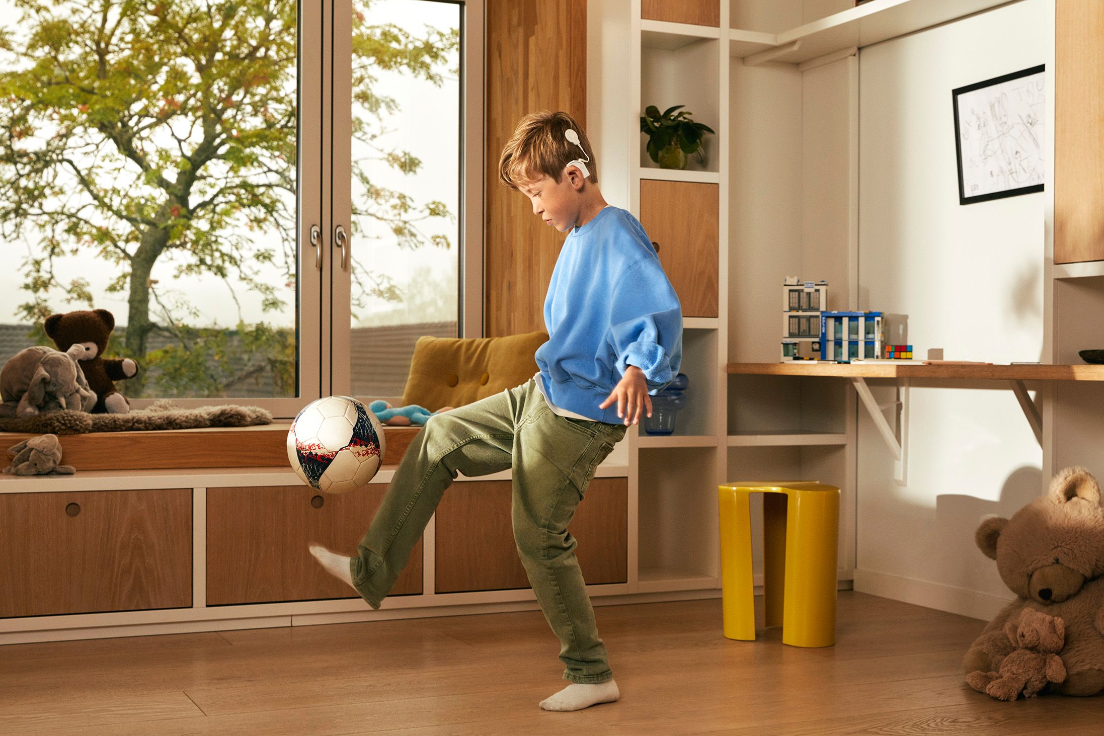 Gutt med cochleaimplantat trikser med en fotball i en stue.